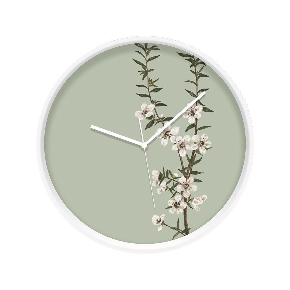 The Vintage Botanical Manuka Wooden Frame Clock - Second features a round wooden frame, pale green face, thin white hands, and a branch with white Manuka flowers and green leaves inspired by New Zealand’s native flora.