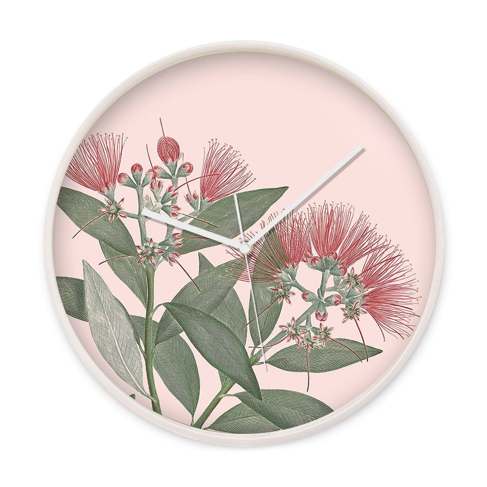 The Vintage Botanical Pohutukawa Wooden Frame Clock displays green leaves and red bottlebrush-inspired flowers on a pale pink background, with white hands and a round, elegant, numberless wooden frame.