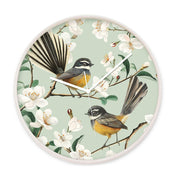 The Chatty Fantails Wooden Frame Clock - Second features two NZ Fantails on blossoming branches with white flowers and a light green background. Designed in New Zealand, it has a light rim, white hands, and a silent movement.