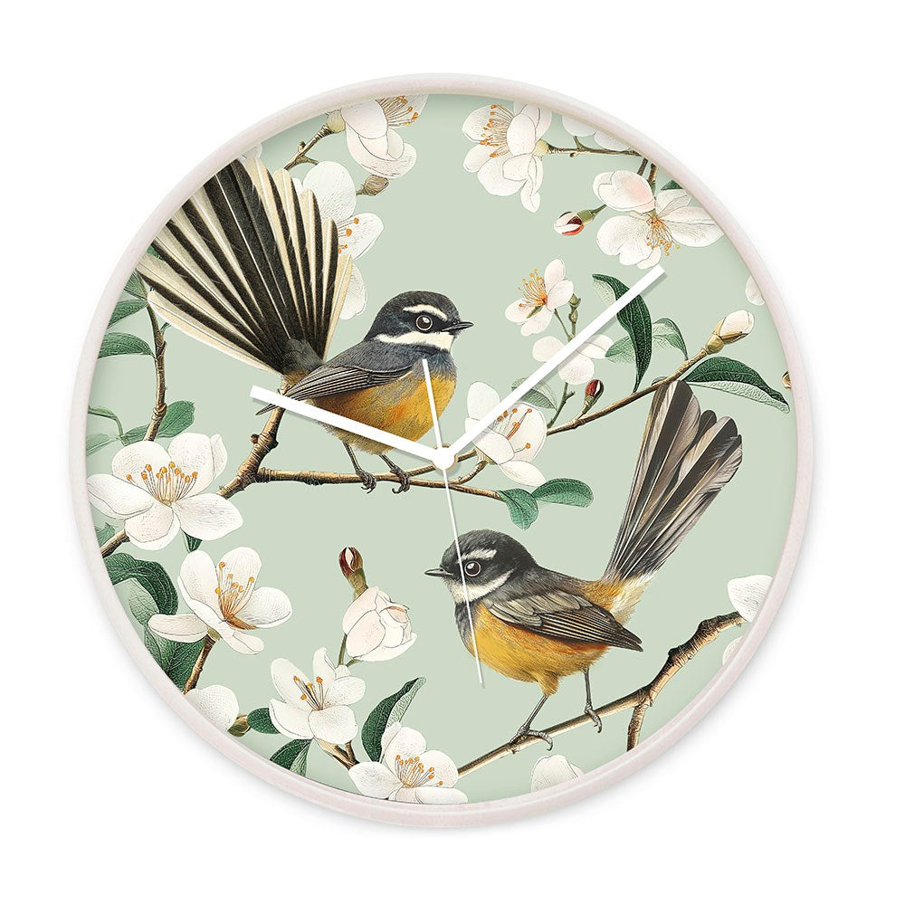 The Chatty Fantails Wooden Frame Clock - Second features two NZ Fantails on blossoming branches with white flowers and a light green background. Designed in New Zealand, it has a light rim, white hands, and a silent movement.