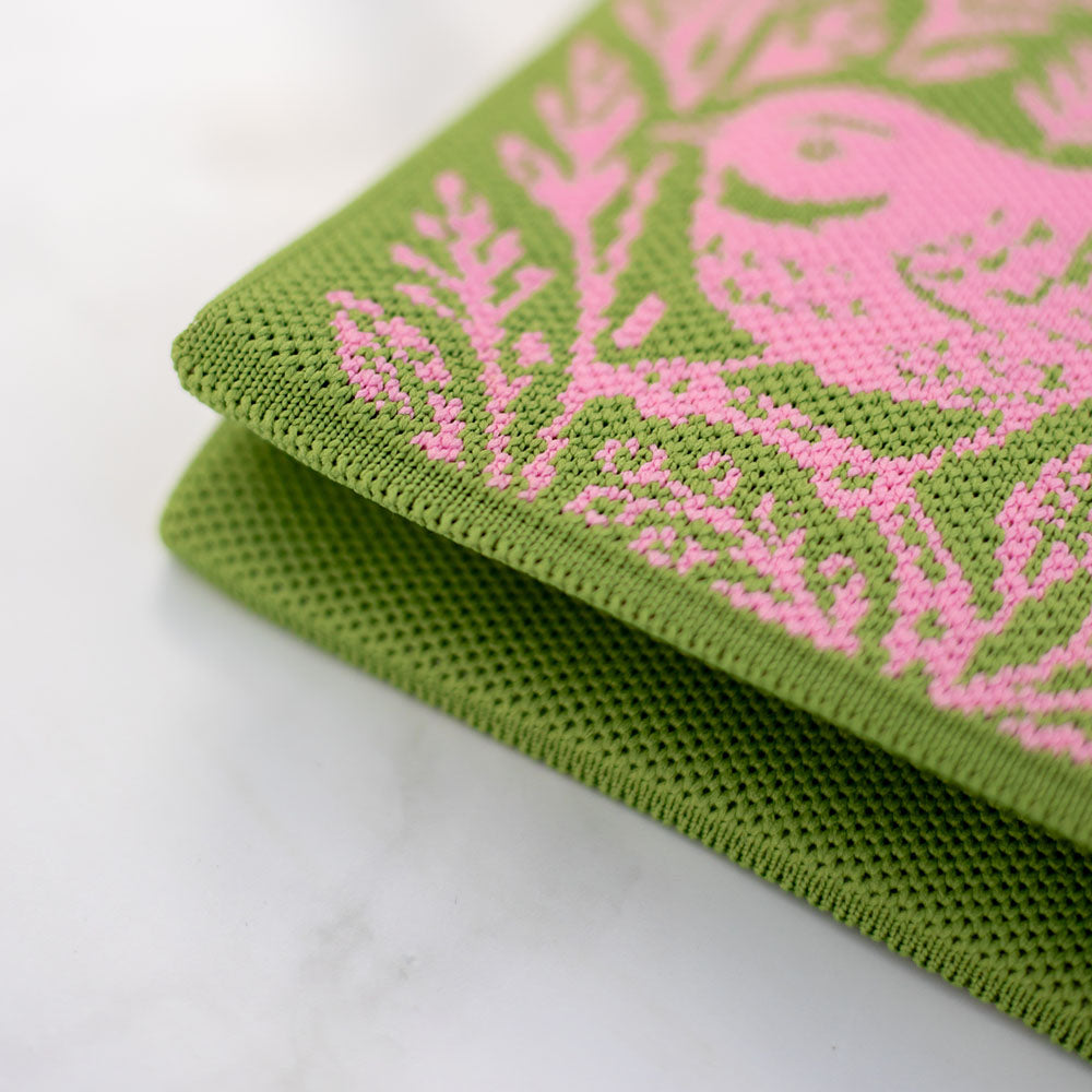 Close-up of two stacked green cloths featuring a pink bird and leaf design inspired by native bird artwork, with visible texture that highlights their suitability for crafting a lightweight Woodcut Fantail Cross-body Mini Bag. Set against a white marble background.