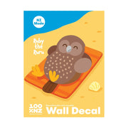 The Ruru Wall Decal features an illustrated brown owl, Ruby the Ruru, lying on an orange beach towel with a seashell nearby. This NZ Made decal offers matte fabric finish and is repositionable—simply peel and stick!.