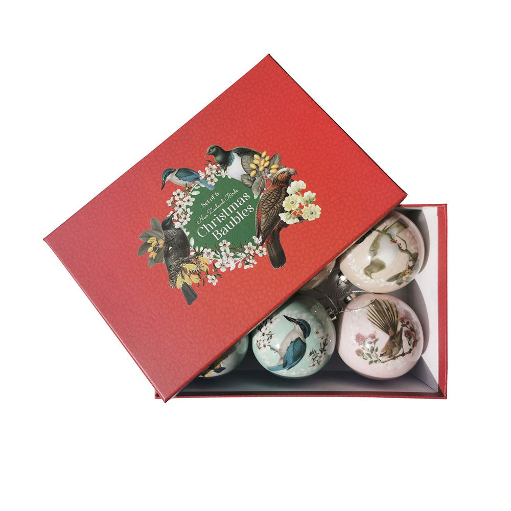 A red box labeled “Box of Six Native Bird Christmas Baubles – Second” contains six baubles featuring native bird designs, adding a Kiwi touch to your decor. The partially open lid displays birds and flowers, revealing the baubles inside.