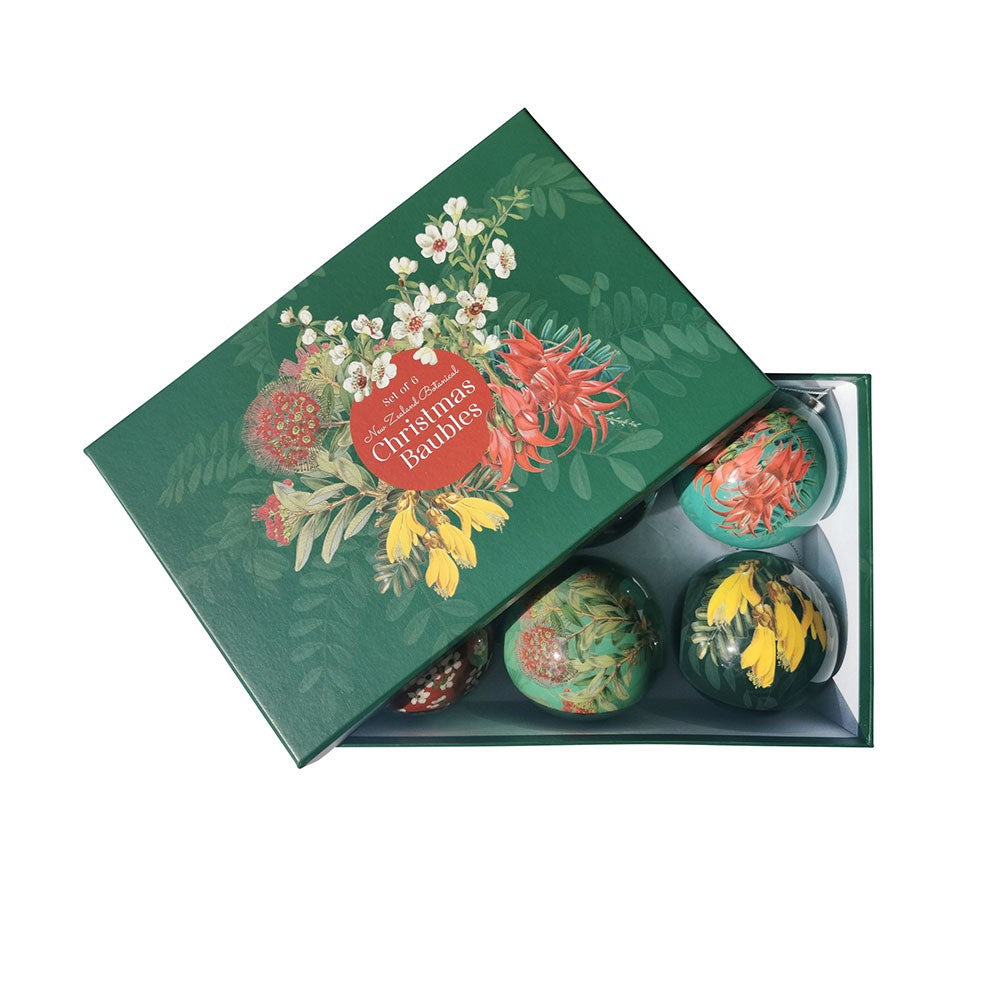 A green box labeled “Box of Six Flora Christmas Baubles - Second,” partially open to reveal six round baubles inside, each decorated with designs inspired by New Zealand native flora. The lid features decorative lettering.