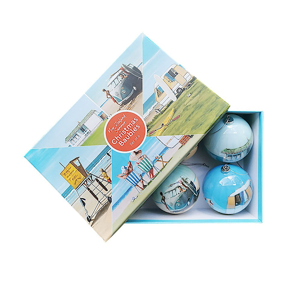 A box of six NZ Summer Christmas baubles—Second features illustrated holiday camping scenes on the lid. The lid is propped open, revealing the lightweight blue decorations inside, inspired by Graham Young artworks.