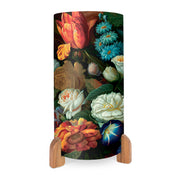 The Vintage Flowers Table Lamp, featuring a cylindrical shape and vibrant floral designs of roses and tulips, is shown on two wooden stands against a white background.