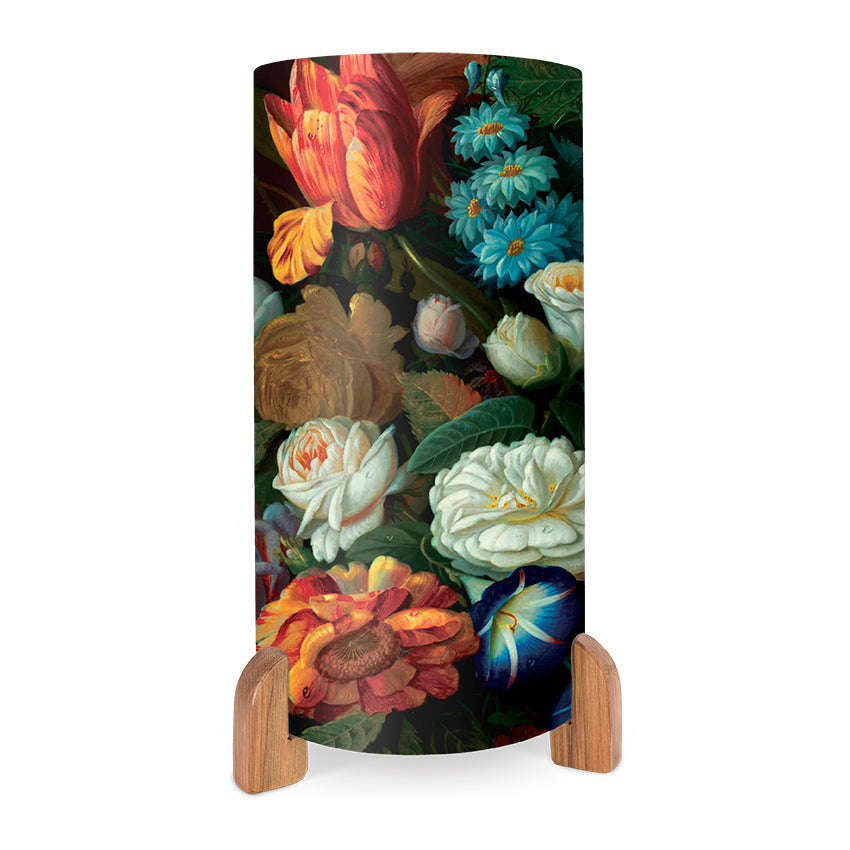 The Vintage Flowers Table Lamp, featuring a cylindrical shape and vibrant floral designs of roses and tulips, is shown on two wooden stands against a white background.