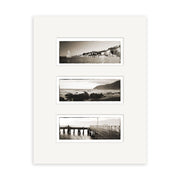 A white mat displays Wellington Triptych - RP105: three horizontal black and white Reuben Price photos—a coastal town, a rocky New Zealand shoreline, and people on a pier.