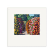 The Karl Maughan - Waikino Small Art Print features a rectangular scene with a flower-lined path and lush green trees, centered on a white mat. This vibrant print showcases red, pink, orange, and purple blooms in a classic Maughan landscape.