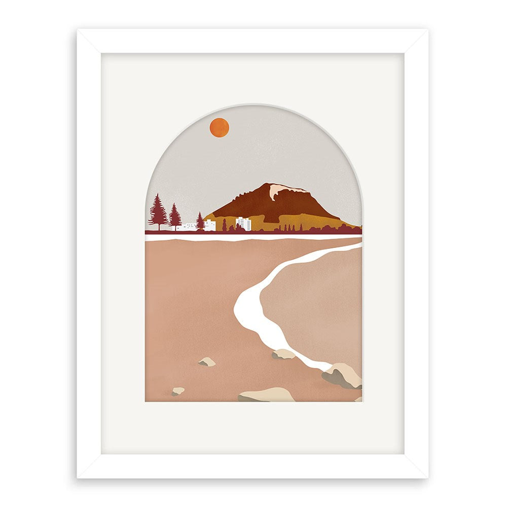 The Mt Maunganui Landmark Art Print features a mountain landscape with reddish-brown tones, trees, and a river under an orange sun, all viewed through an arched window shape. Comes framed in white.