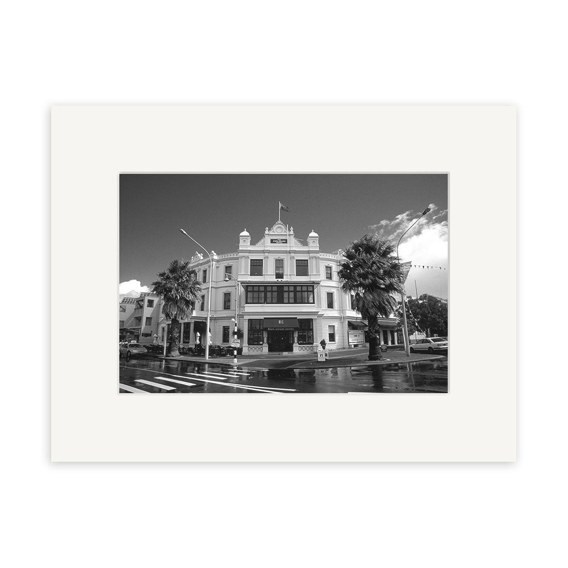 Black and white photo titled Devonport Esplanade - RP023 shows a historic three-story building with columns and a flag, on a palm-lined street in New Zealand—ideal for photographic prints on archival quality paper.