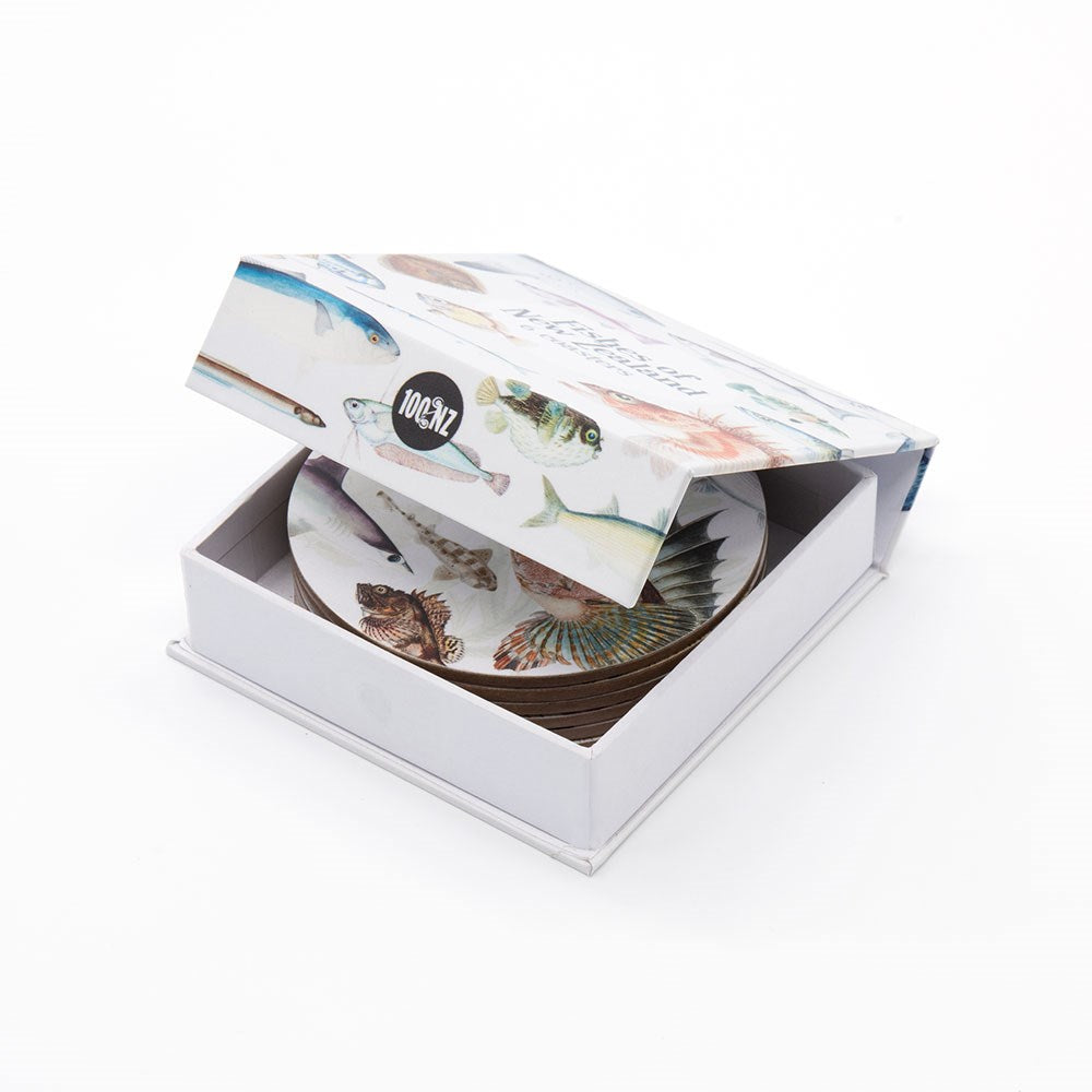 A white box labeled 100% NZ contains the Fishes of NZ Set of 6 Coasters. The open box reveals round coasters, each decorated with illustrated New Zealand fish designs matching the artwork on the box.