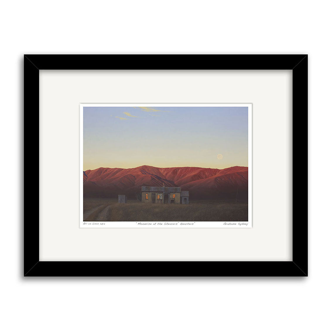Grahame Sydney - Moonrise at the Shearers Quarters Small Art Print features a small house with lit windows among red hills beneath a dusky sky and moon, presented in a black frame with white mat and handwritten text.