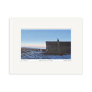 Grahame Sydney - Dusk at Shearers Kitchen Small Art Print: A solitary stone building in snowy open land at sunset, with warm light on the horizon and figures near the structure, evoking the artists signature style.