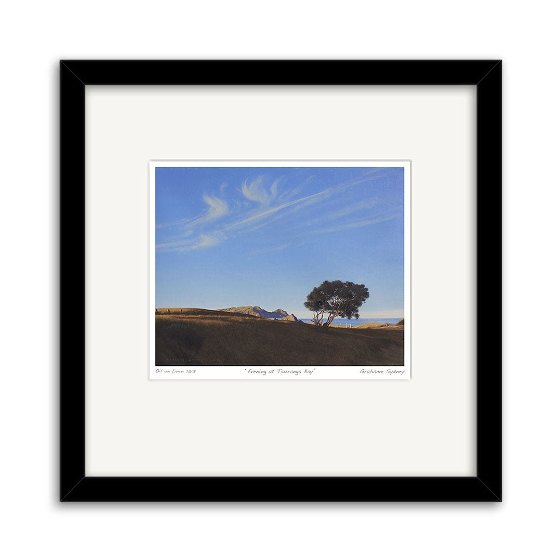 The Grahame Sydney - Evening at Tauranga Bay Small Art Print features a single tree in a grassy field beneath a blue sky with wispy clouds and distant hills, centered with a white mat and black frame—print available.