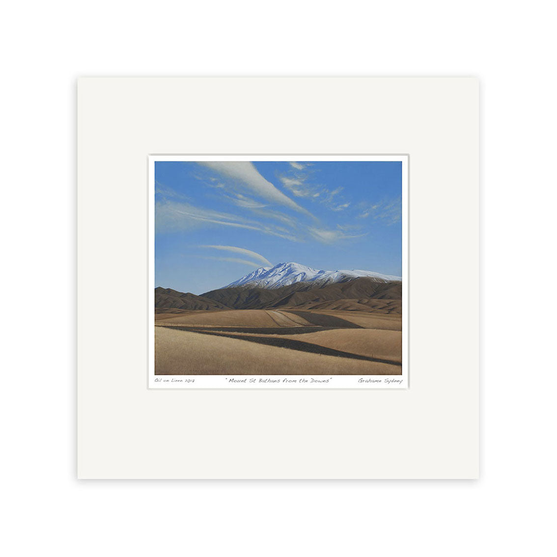 The Grahame Sydney - Mt St Bathans from the Downs Small Art Print features a snow-capped mountain, brown rolling hills, and a blue sky with wispy clouds, centered on white mat board. Prints available.