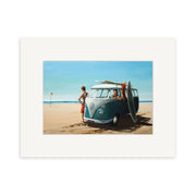 The Graham Young - Surf Wagon Small Art Print features a vintage blue Volkswagen van on a sandy beach with the ocean in the background, one person inside, another outside, and a surfboard leaning against the van. Available as art prints.