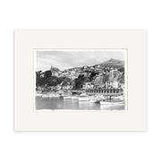 Oriental Bay 1929 - HI001: Black and white photo of a New Zealand coastal town with docked boats, hillside buildings, and a church. Presented as a historical photographic print on archival matte paper with white mat border.