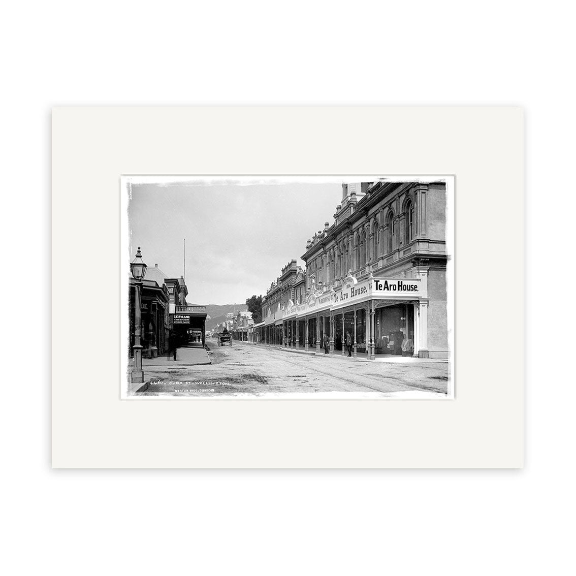 Black and white photo titled Cuba St 1888 - HI002 shows a New Zealand city street lined with multi-story buildings, including visible “Te Aro House” signs, an old-fashioned streetlamp, and is printed on archival quality matte paper.