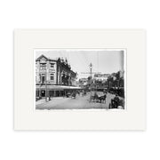 Lambton Quay 1900 - HI003: Archival black and white photo of a New Zealand city street with horse-drawn carriages, pedestrians, multi-story buildings, and an old streetlight.