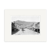 Black-and-white photo titled Courtenay Place 1900 No.1 - HI006 shows a wide New Zealand street with trolley tracks, buildings, a mountain backdrop, few pedestrians, and streetcars. Historical Photographic Print on archival matte paper.