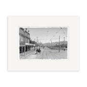 The Kent Terrace 1900 - HI008 is a black and white historical photographic print of a street with trolley tracks, early cars, storefronts, and mountain views. Printed on archival quality matte paper in New Zealand.