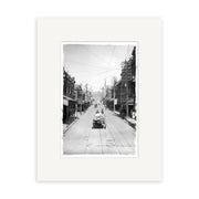 Willis St 1900 - HI013: Black-and-white historic city street photo with trolley tracks, early cars, pedestrians, and buildings (some under construction); hills in the distance. Printed on archival quality matte paper.