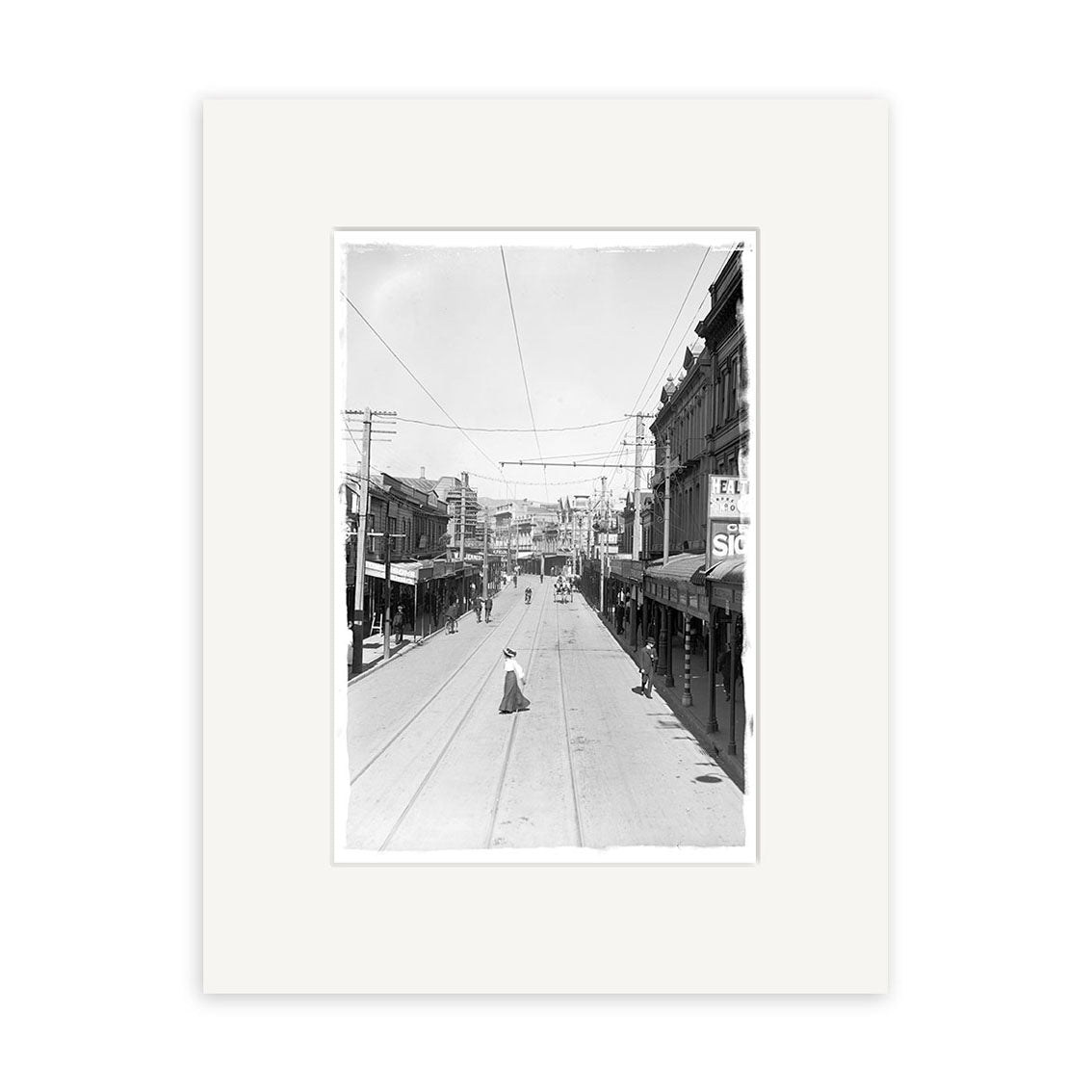 Manners St 1907 - HI014: Black and white photo of a wide street with buildings, shops, a few people, and trolley tracks. This historical print is made on archival quality matte paper.