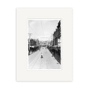 Manners St 1907 - HI014: Black and white photo of a wide street with buildings, shops, a few people, and trolley tracks. This historical print is made on archival quality matte paper.