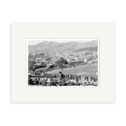 Black and white photo, Basin Reserve 1900 - HI016: cricket match in progress with players on the field, spectators in hats, buildings and hills behind. Archival quality matte paper, made in New Zealand.