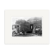 Archival black-and-white photo, Upper Hutt 1920 - HI017: a truck with hay bales and a horse-drawn cart outside an Upper Hutt building; two men by the truck, one on the cart with two horses. Made in New Zealand.
