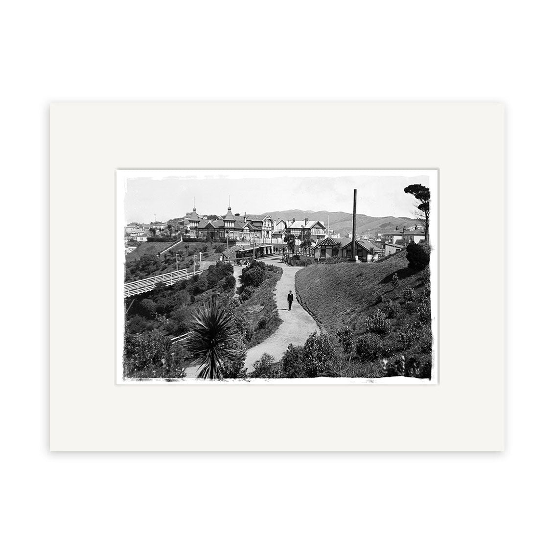 Kelburn Car 1918 - HI018: Black and white photo featuring a vintage car on a hilly road, surrounded by lush plants and Victorian houses, expertly reproduced on archival-quality matte paper.