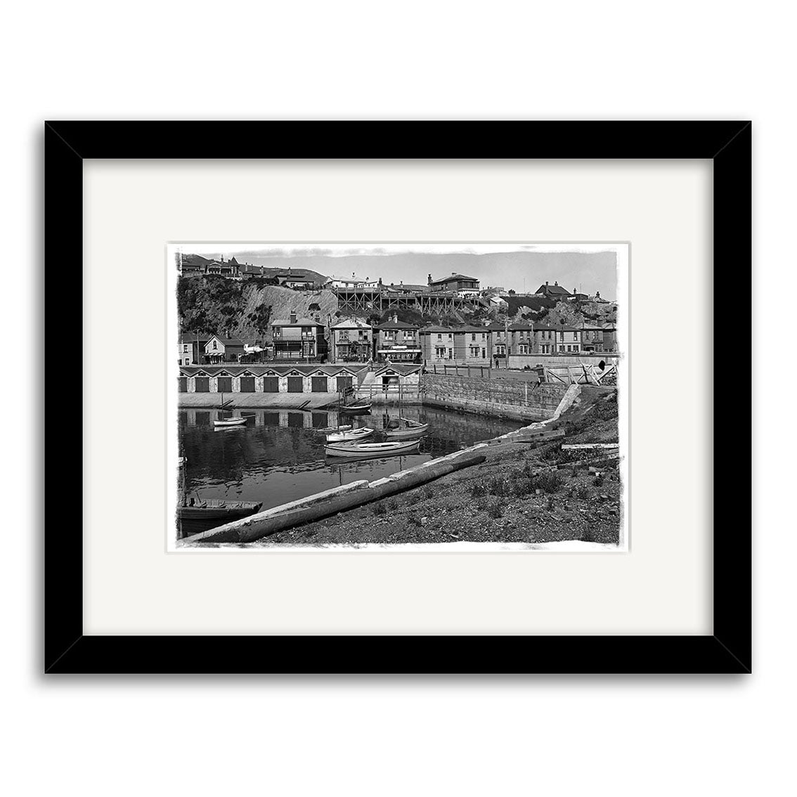 Archival quality black and white photo titled Oriental Bay 1910 - HI020, featuring a New Zealand coastal town with boats, beach huts, and hillside houses; framed and matted as a Historical Photographic Print for display.