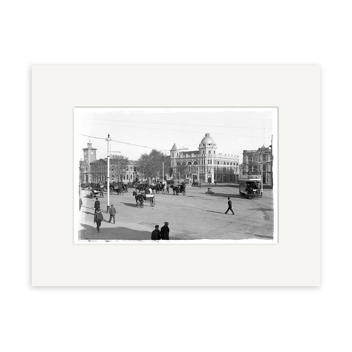 Cathedral Square 1910 - HI026: Archival quality black and white photo depicting a bustling early 20th-century New Zealand city street with pedestrians, horse-drawn carriages, vintage cars, and a domed building in the background.