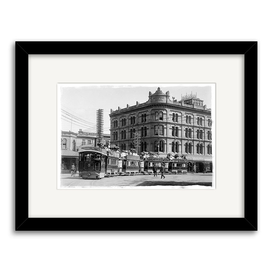 Beautifully framed Puffing Billy 1902 - HI027: a black and white historical photographic print of an old New Zealand city street with two trams, people, and a grand building, printed on archival matte paper with white mat and black frame.