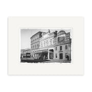 Archival-quality black-and-white photo, Tuam St 1900 - HI030, shows a historic New Zealand street with a three-story brick building, smaller storefront, Whites Depository sign, people near the entrance, and a streetcar to the left.