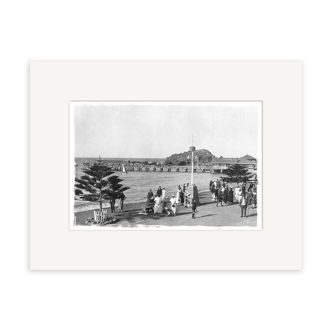 Black and white historical photographic print titled Sumner Christchurch - HI031, showing people walking along a waterfront promenade with a pier, distant hill, and buildings. Printed on archival quality matte paper and framed with a white mat.