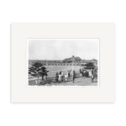 Black and white historical photographic print titled Sumner Christchurch - HI031, showing people walking along a waterfront promenade with a pier, distant hill, and buildings. Printed on archival quality matte paper and framed with a white mat.