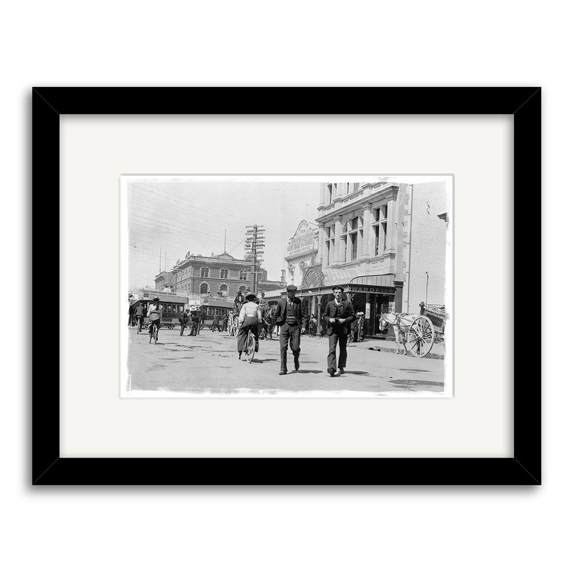 Cnr High & Cashel St - HI032: Black and white photo print of a bustling early 1900s street scene with people, carriages, and historic buildings; archival matte paper, white mat, black frame.
