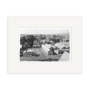 Worcester St 1882 - HI033: Black and white photo of a New Zealand town featuring buildings, trees, dirt roads, a horse-drawn cart at the bottom right, and hills in the background beneath a partly cloudy sky.