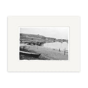 Moncks Bay 1914 - HI034: Black and white photo of a calm New Zealand waterfront with boats, docks, hills, buildings, and church spire. Historical print displayed with a white mat.
