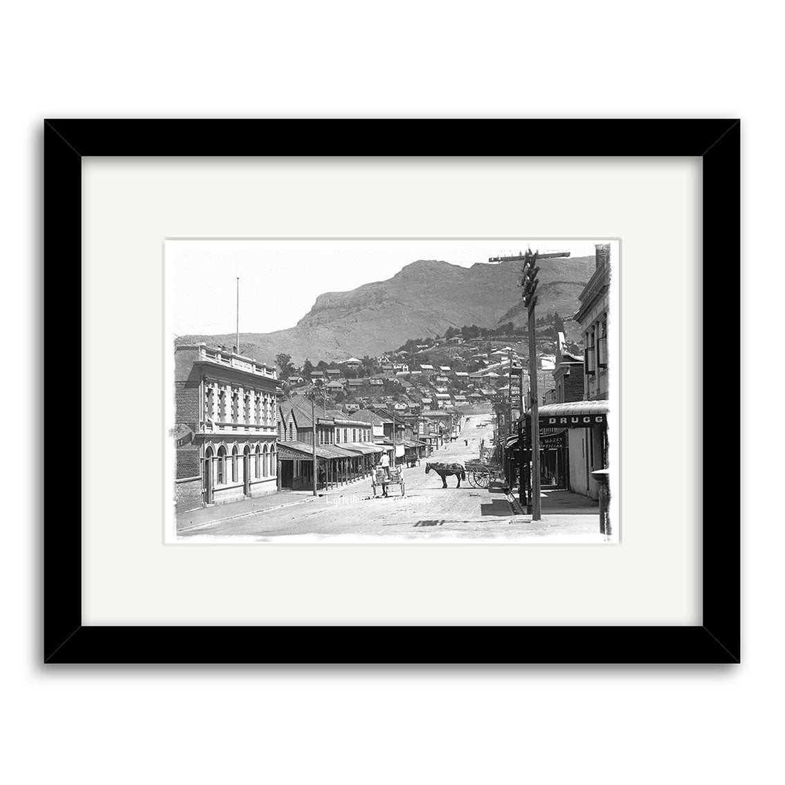 Black and white historical photographic print, London St Lyttelton 1916 - HI037, shows a New Zealand town street with horse-drawn carriages. Framed in black with a white mat, printed on archival quality matte paper for lasting elegance.