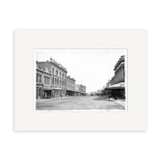 Black and white photo, Queen St 1880 - HI040, shows a wide empty street in New Zealand lined with multi-story buildings featuring awnings and ornate details. This historical photographic print is archival quality for collectors and enthusiasts.
