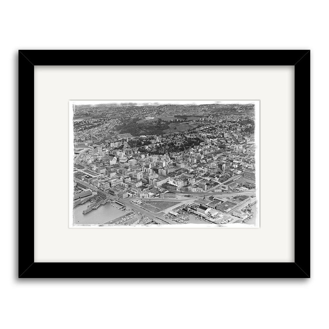 Auckland City 1939 - HI041: A black-and-white aerial photo of Auckland with harbor, buildings, and green spaces as a historic archival print, displayed in a wide white mat and simple black frame.