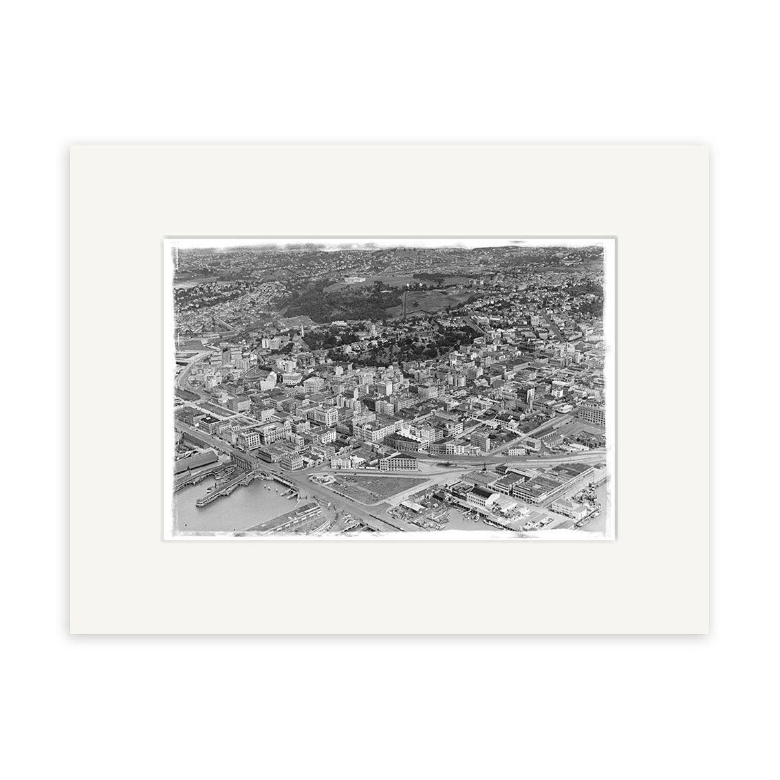 Auckland City 1939 - HI041: An exquisite archival-quality black and white aerial photographic print of Auckland city, featuring buildings, streets, and water in the lower left, elegantly presented with a wide white mat frame.