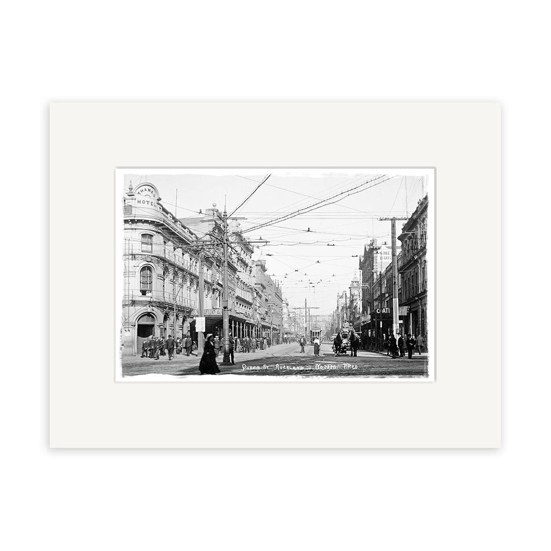 Archival quality black-and-white photo, Queen Street Auckland - HI042, shows a 1904 New Zealand city scene with people, horse-drawn carriages, streetcars beneath wires, and multi-story buildings lining the road.