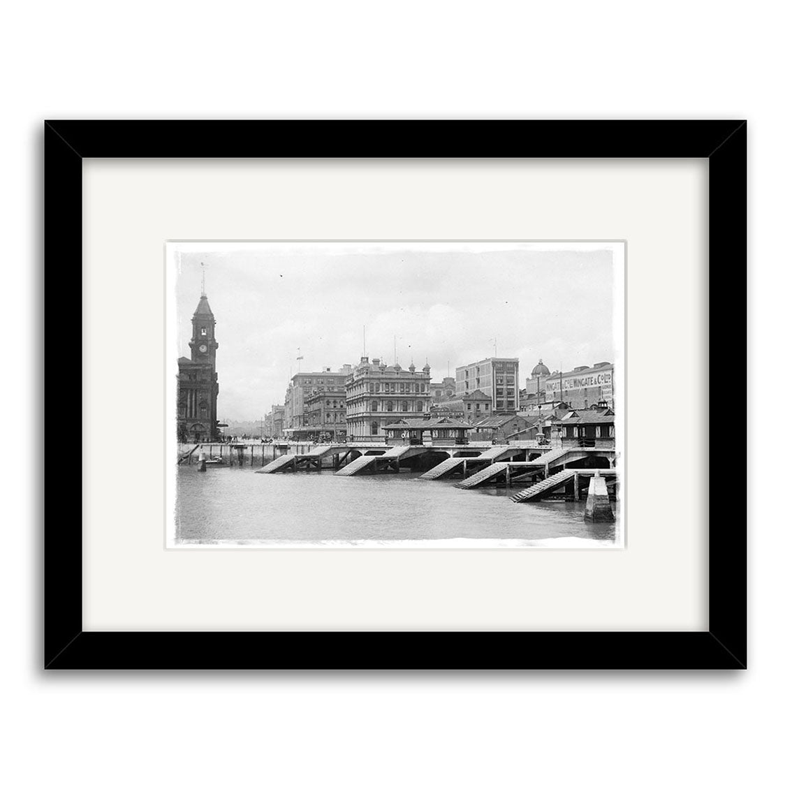 Archival-quality black and white photographic print Auckland Water Front 1916 - HI043, featuring a city waterfront, bridge, historic buildings, and clock tower; presented with a black frame and white mat.
