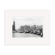 Archival-quality black and white photographic print, “Auckland Water Front 1916 - HI043,” shows a New Zealand cityscape with a river, bridge, large buildings, and a clock tower on the left, all bordered by a white matte.