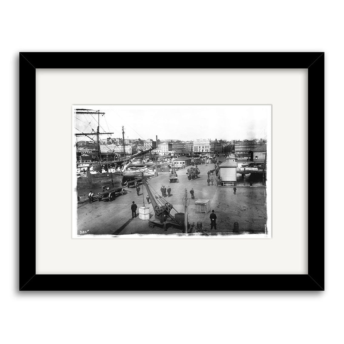 Queens Wharf 1905 - HI045 is a black and white archival photo, framed with a white mat and black border, depicting a busy 1905 New Zealand street with people, horse-drawn carriages, early cars, and historic buildings.