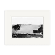 St Georges Bay 1864 - HI049 is a black and white photo of calm water with distant islands, framed by trees and a white fence. This historical print is mounted with a white mat on archival quality matte paper.